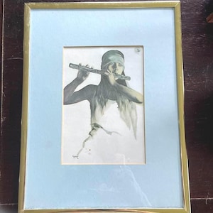 May include: A framed artwork featuring a monochromatic illustration of a person playing a flute. The figure wears a headband and a simple top. The piece is set within a light blue mat and a thin gold-toned metal frame, with a small signature visible.