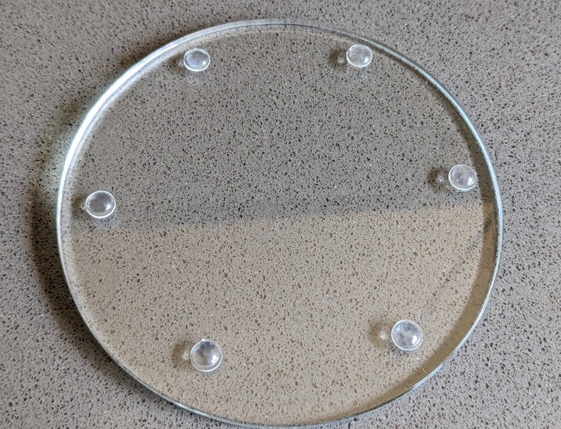 Pu&ograve; includere: Un sottobicchiere rotondo in vetro trasparente con cinque piedini in gomma sul fondo.