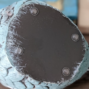 May include: The underside of a light blue ceramic figurine with a dark brown base. The base has four rubber feet to prevent scratching.