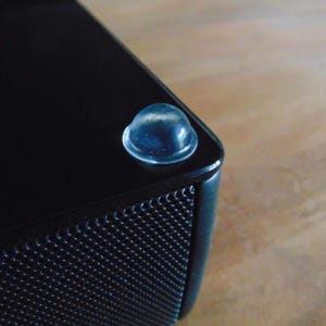 May include: Close-up of a black speaker with a clear rubber foot on the corner.