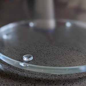May include: A clear glass coaster with four small rubber feet on the bottom.
