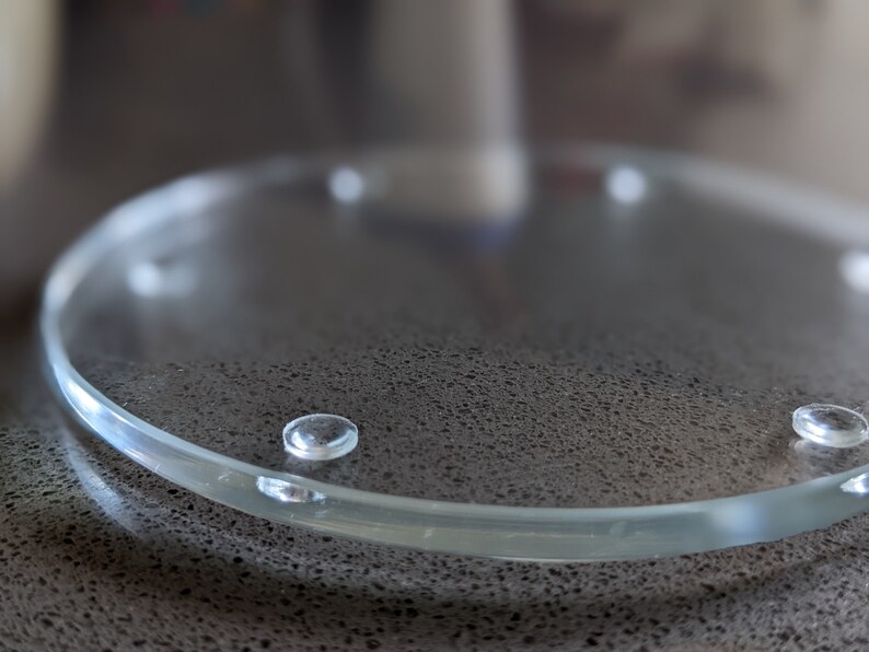 May include: A clear glass coaster with four small rubber feet on the bottom.