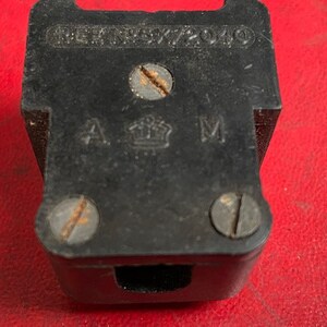 Könnte beinhalten: Eine schwarze Steckdose aus Kunststoff mit dem Text "REG. NSY 72040" und "A M" mit einem Kronensymbol dazwischen.