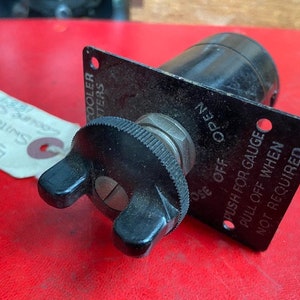 May include: A black metal switch with a round knob and two levers. The switch has the text "OPEN", "OSE OFF", "PUSH FOR GAUGE", "PULL OFF WHEN", and "NOT REQUIRED" printed on it.
