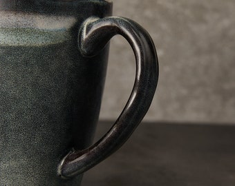 May include: A dark blue ceramic mug with a textured finish and a black handle. The mug has a slightly flared rim.