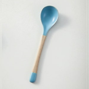 May include: A light blue ceramic spoon with a beige handle. The spoon is ideal for serving soup, cereal, or other dishes.