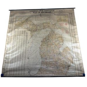 May include: Vintage map of Michigan by National Map Company, featuring detailed road networks and geographical features. The map is printed on aged paper and mounted on a black rod with blue end caps. The text "MAP OF MICHIGAN" is visible at the top.