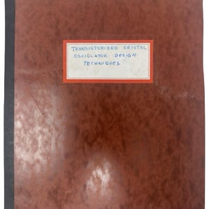 May include: A brown notebook with a black spine. A white label with blue text reads "TRANSISTORIZED CRYSTAL OSCILLATOR DESIGN TECHNIQUES". The notebook has a textured, mottled appearance.