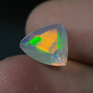 May include: A triangular cut opal gemstone with a white body color and iridescent flashes of green, orange, and yellow.