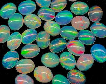 Puede incluir: Colección de ópalos ovalados con colores iridiscentes de azul, verde, rojo y amarillo. Los ópalos están sobre un fondo negro, mostrando su vibrante juego de colores. Estas piedras preciosas pulidas son aptas para la fabricación de joyas.