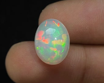 Puede incluir: Una piedra preciosa de ópalo ovalada blanca con un arcoíris de colores, incluyendo rojo, naranja, amarillo, verde y azul.