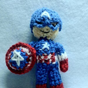 May include: A crocheted Captain America doll with a red, white, and blue costume and a red, white, and blue shield.