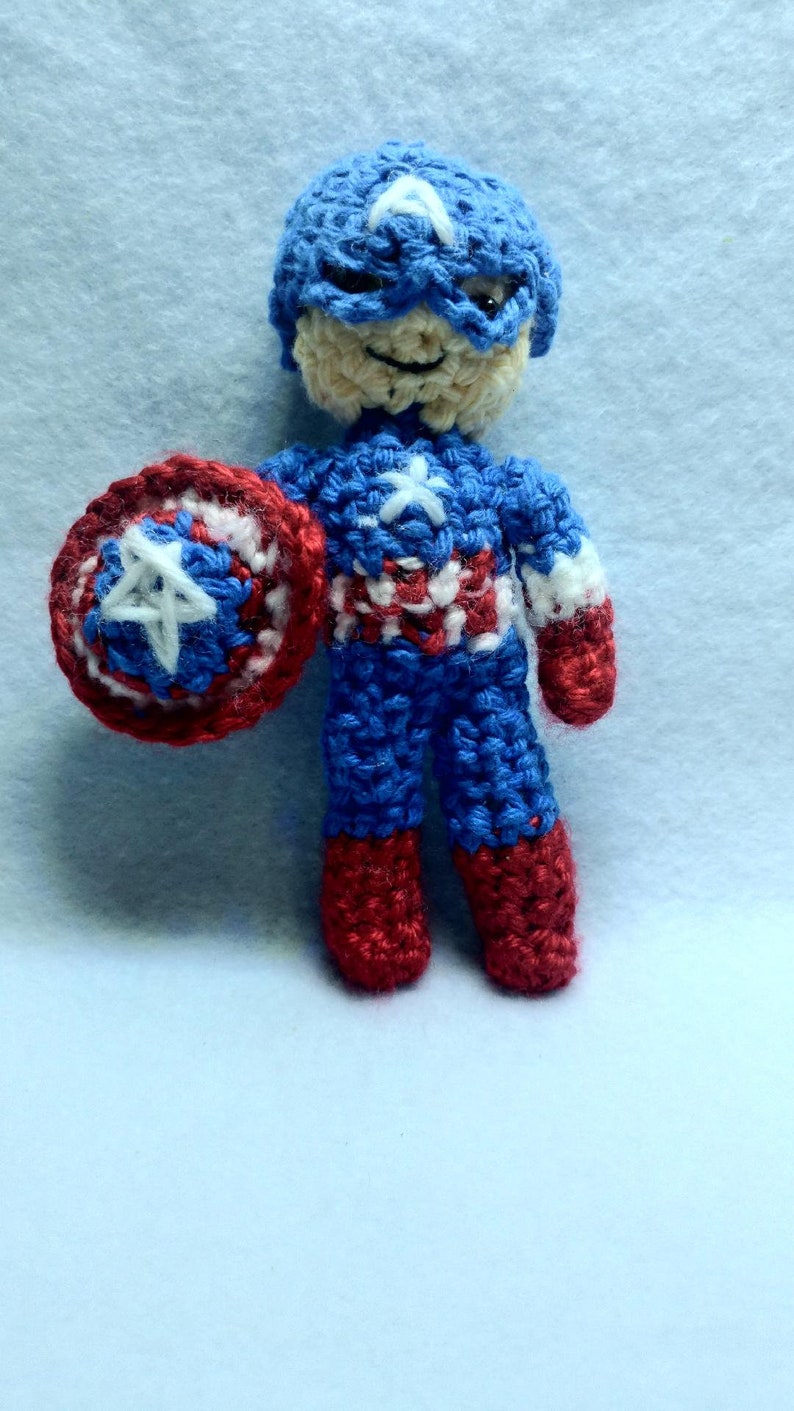 May include: A crocheted Captain America doll with a red, white, and blue costume and a red, white, and blue shield.