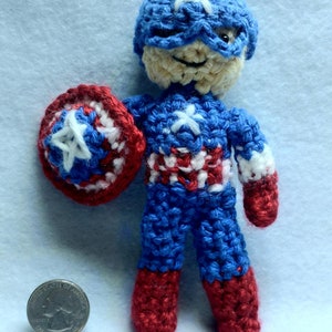 May include: A crocheted Captain America doll with a red, white, and blue costume, holding a red, white, and blue shield. The doll is about the size of a quarter.