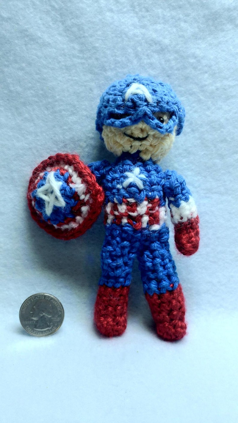 May include: A crocheted Captain America doll with a red, white, and blue costume, holding a red, white, and blue shield. The doll is about the size of a quarter.