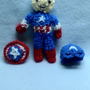 May include: A crocheted Captain America doll with a red, white, and blue costume, a red and blue shield, and a blue hat.