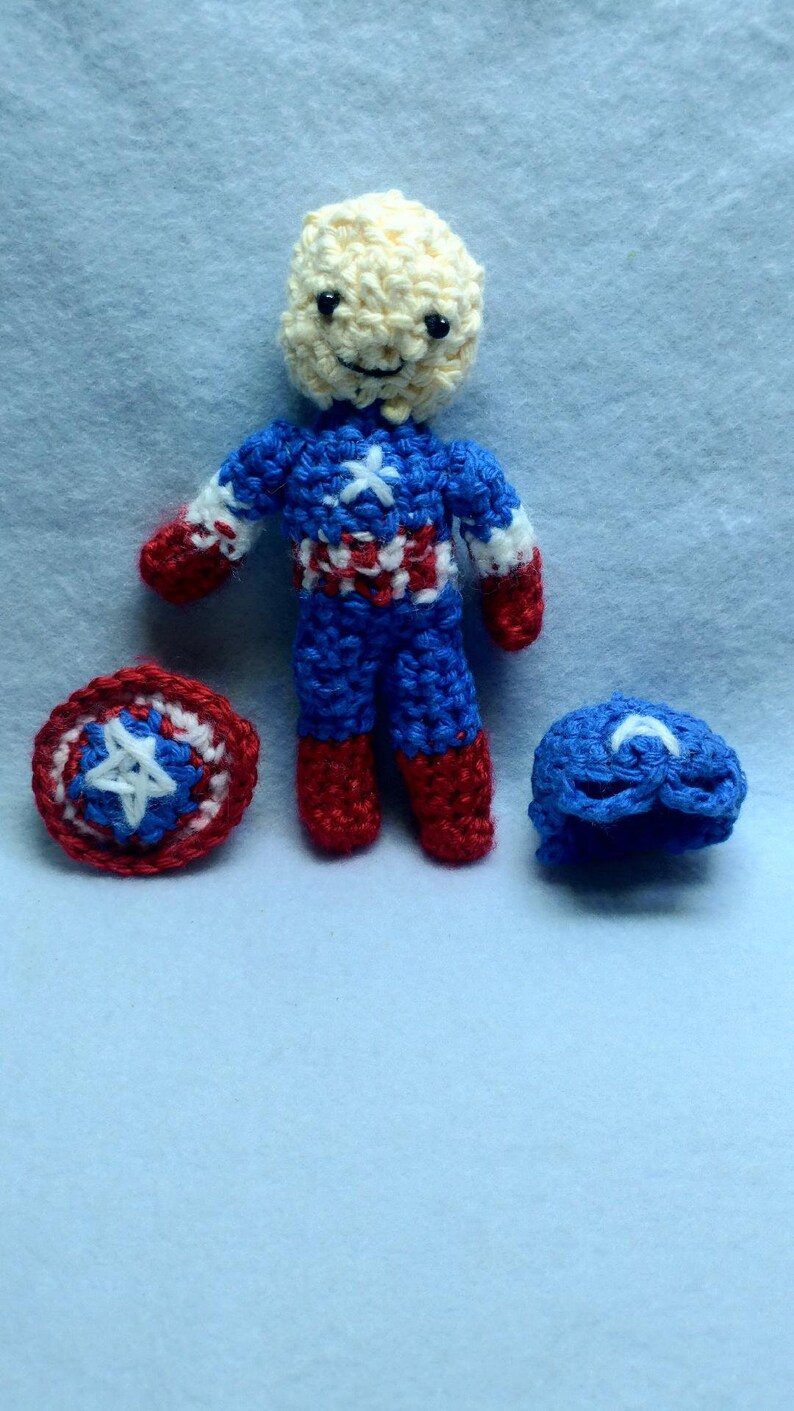 May include: A crocheted Captain America doll with a red, white, and blue costume, a red and blue shield, and a blue hat.