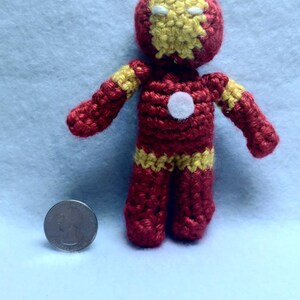 May include: A crocheted red and yellow Iron Man character with a white face and a white circle on the chest. The character is about 4 inches tall.