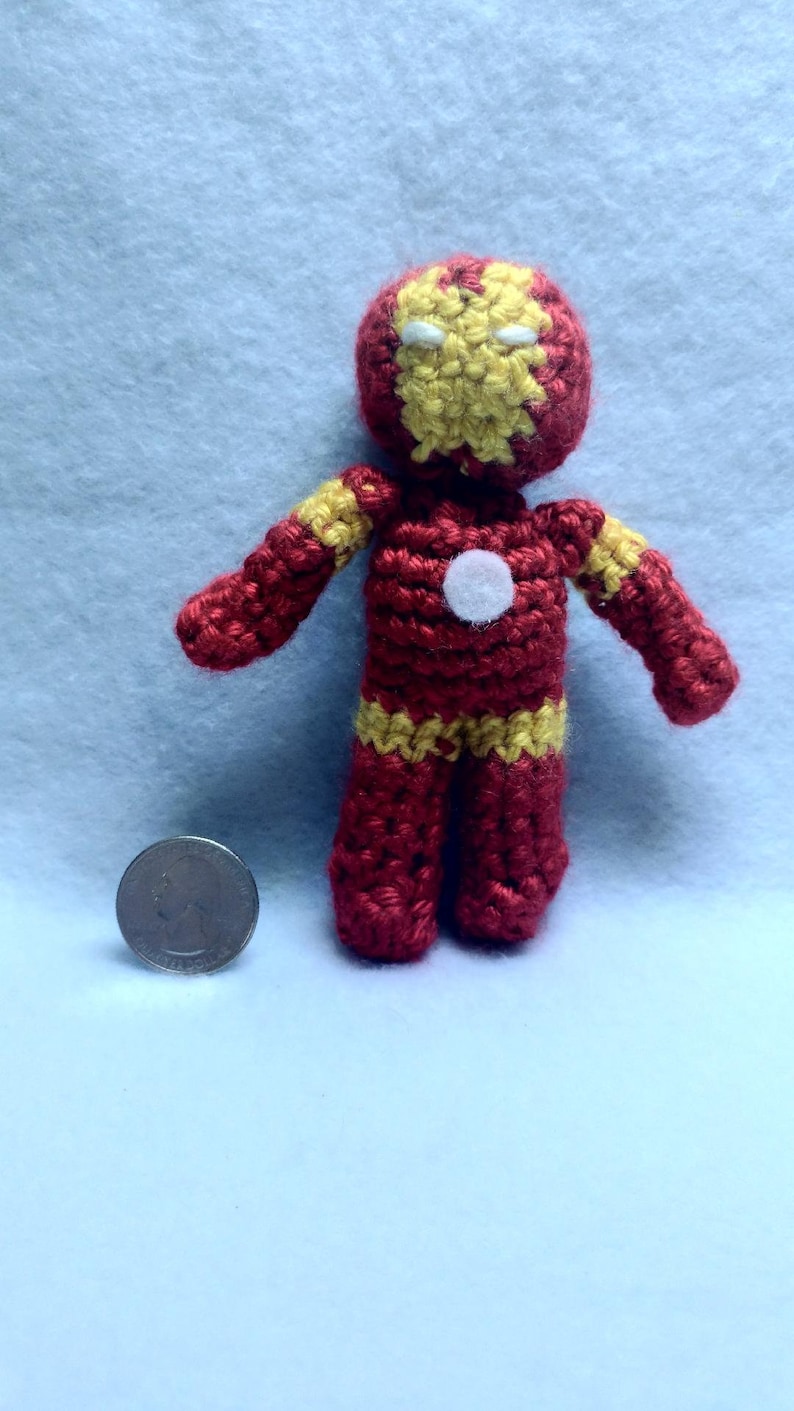 May include: A crocheted red and yellow Iron Man character with a white face and a white circle on the chest. The character is about 4 inches tall.