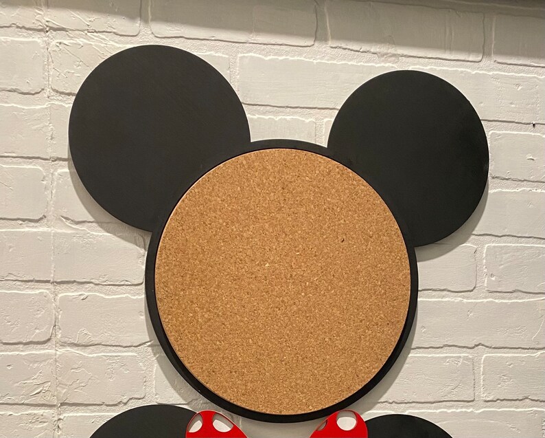 May include: A corkboard shaped like Mickey Mouse's head with black ears and a brown cork centre.