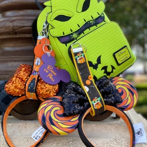 May include: A lime green backpack with a stitched design, a black bat, and a Disney Loungefly tag. A pair of black and orange Mickey Mouse ears with a sequined bow and a lollipop design. A keychain with a Baby Yoda design.