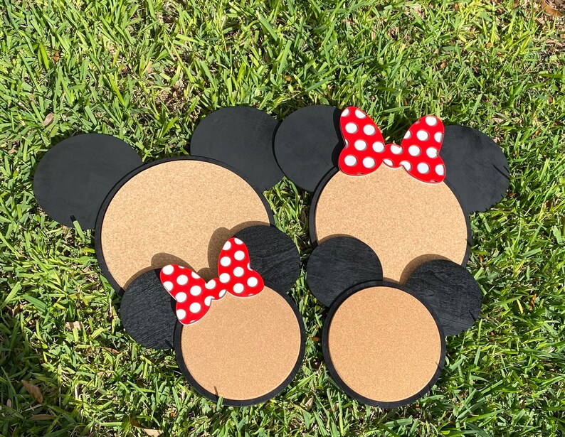 May include: Three corkboard mouse head shapes with red and white polka dot bows. The mouse heads are black with corkboard centres.