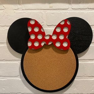 May include: A black and red Minnie Mouse-themed corkboard with a round cork centre and black ears with a red bow with white polka dots.