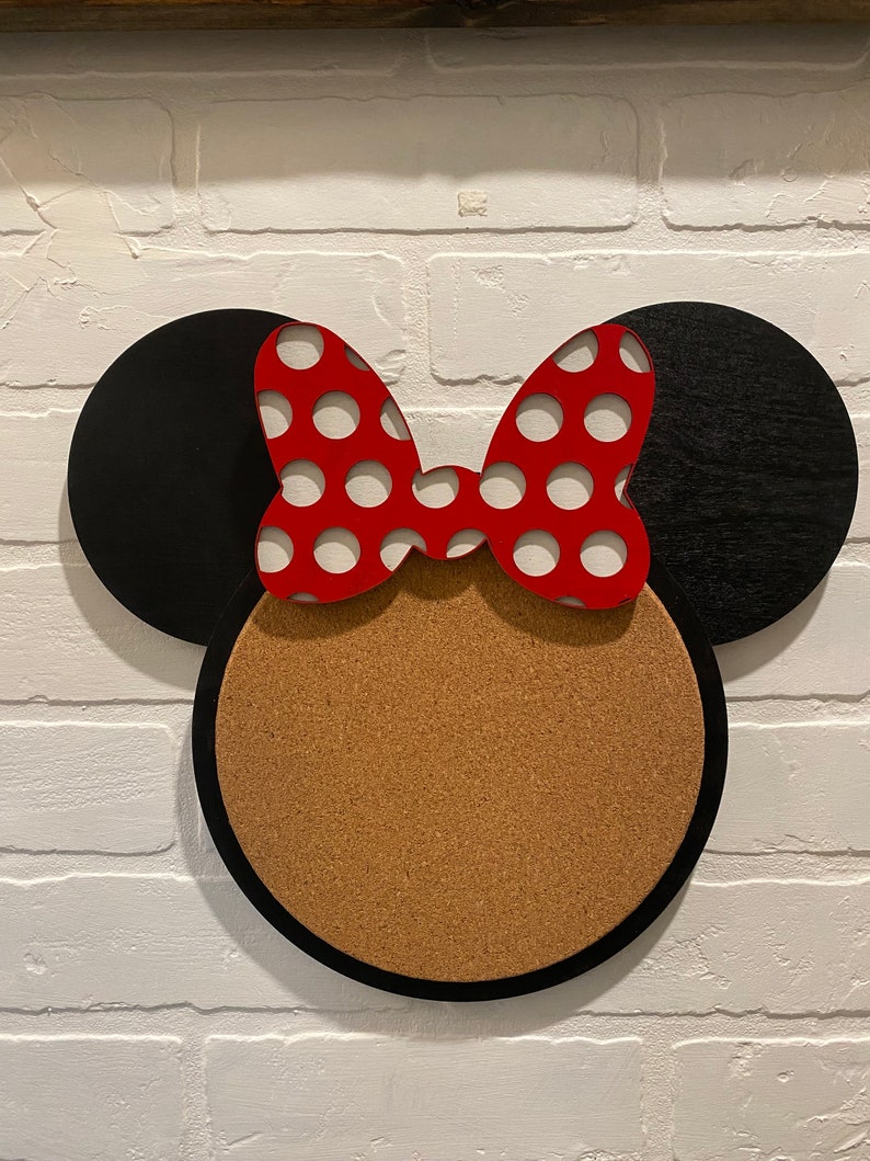 May include: A black and red Minnie Mouse-themed corkboard with a round cork centre and black ears with a red bow with white polka dots.