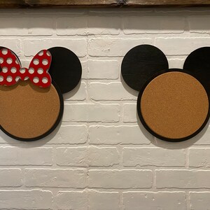 May include: Two corkboard notice boards shaped like Mickey Mouse and Minnie Mouse heads. The Minnie Mouse board has a red and white polka dot bow.