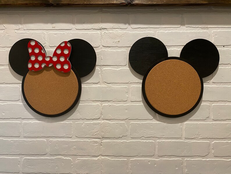 May include: Two corkboard notice boards shaped like Mickey Mouse and Minnie Mouse heads. The Minnie Mouse board has a red and white polka dot bow.