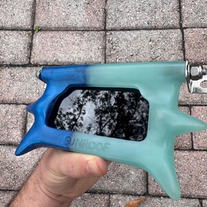 May include: A blue and teal sunroof tool with the word "SUNROOF" printed on the side. The tool has a star-shaped design on the end and a metal hinge.
