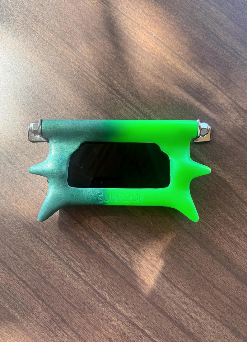 May include: Green and black sunglasses with a distinctive, angular design. The frame features a gradient of green hues, with a dark lens. The text "SUNROOF" is visible on the frame. The sunglasses have a modern aesthetic.