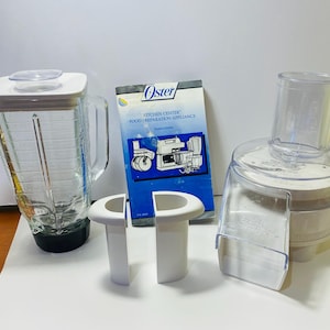 Puede incluir: Un juego de electrodomésticos de preparación de alimentos Oster Kitchen Center. El juego incluye una licuadora de vidrio con tapa blanca, un procesador de alimentos con un recipiente de plástico transparente y un manual. El manual tiene el logotipo de Oster.