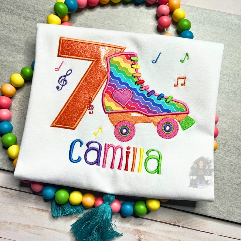 May include: A white t-shirt with an orange number 7, a rainbow roller skate with a pink heart, and the name "camilla" embroidered in colorful thread.