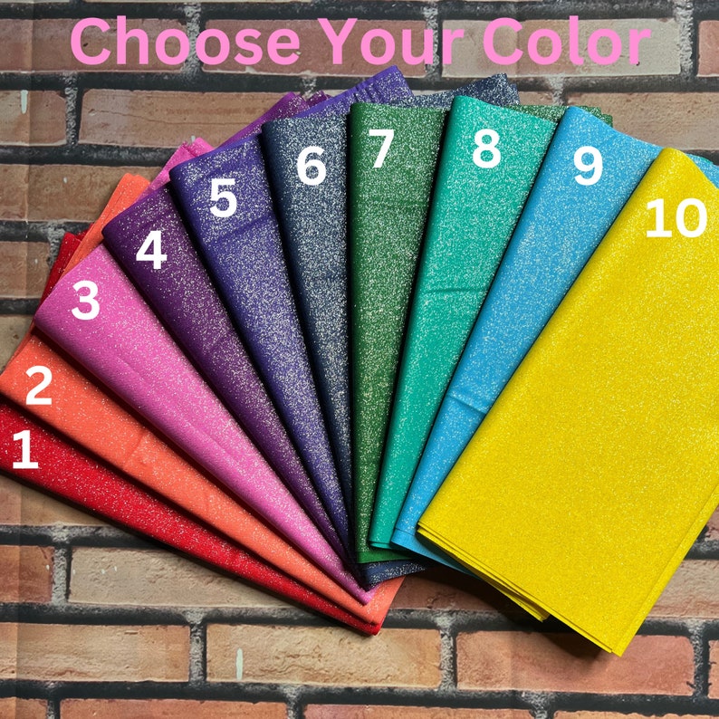 May include: Ten swatches of glitter fabric in various colors, including red, orange, pink, purple, blue, green, and yellow. The fabric is arranged in a fan shape with the numbers 1 through 10 printed on each swatch. The text "Choose Your Color" is printed at the top of the image.