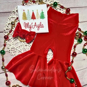 May include: Red velvet bell bottom pants with a white shirt featuring a row of embroidered Christmas trees and the name "My Ayla".