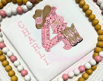 May include: A white t-shirt with pink embroidery of the number four, a cowboy hat, and boots. The name "CHARLI" is embroidered vertically on the left side of the shirt.