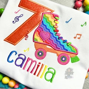 May include: A white t-shirt with a rainbow roller skate, a glittery orange number 7, and the name "camilla" embroidered in rainbow colors.