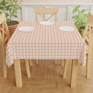May include: A peach-coloured gingham tablecloth with white squares covers a wooden table with four chairs. Two white plates are placed on the table.
