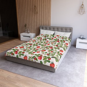 May include: A white duvet cover with a repeating pattern of red strawberries and green leaves. The duvet cover is on a bed with white pillows and a gray headboard.