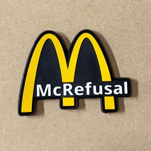 Może przedstawiać: Żółto-czarna parodia logo McDonald's z napisem "McRefusal" w kolorze białym.