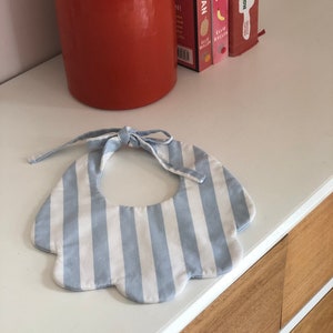 May include: A blue and white striped baby bib with a scalloped edge and a tie closure.