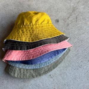 May include: A stack of six bucket hats in various colors, including yellow, brown, pink, blue, and green.