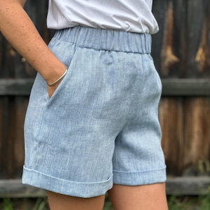 以下が含まれることがあります： 幅広のゴムウエストとカフ付きの裾が付いた、薄いブルーのリネン製ショートパンツです。