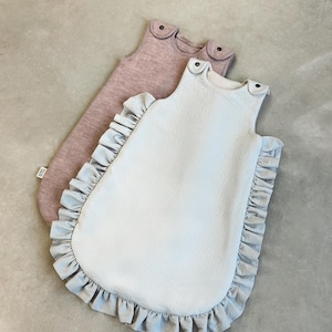 May include: Two baby sleep sacks, one light blue with ruffles and one dusty rose. Both sleep sacks have a sleeveless design.