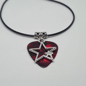 Può includere: Una collana con un plettro per chitarra rosso e un ciondolo a forma di stella argentata. Il plettro è attaccato a un cordino nero.