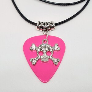May include: A pink guitar pick necklace with a silver skull and rhinestone accents.
