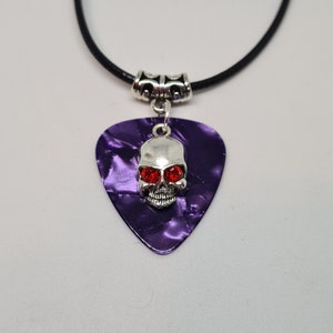 May include: A purple guitar pick necklace with a silver skull pendant featuring red rhinestone eyes.