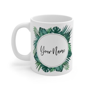 Può includere: Tazza in ceramica bianca con un design a foglie tropicali verdi e un cerchio al centro che dice "Your Name".