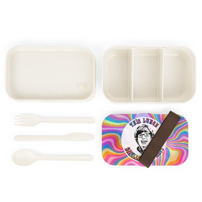 Puede incluir: Una fiambrera blanca con un dise&ntilde;o psicod&eacute;lico colorido que presenta la cara de un hombre y el texto "This Lunch Swells My Soul". La fiambrera incluye una tapa a juego, una correa marr&oacute;n y un juego de cubiertos blancos.